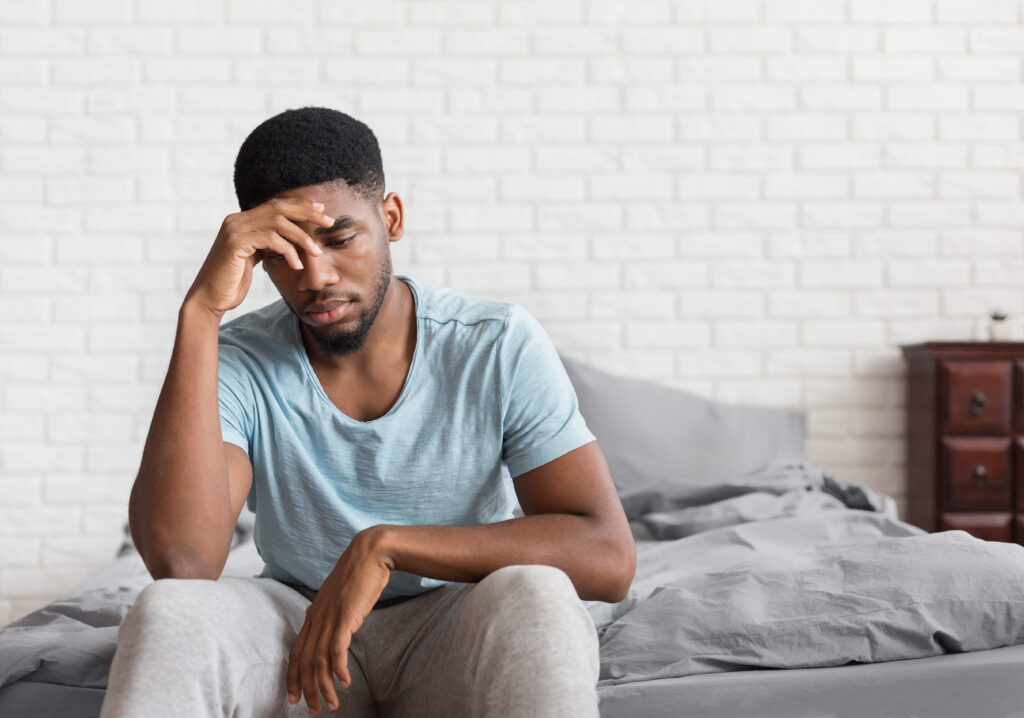 Young depressed black man sitting on bed - NinjaFitness Bad mood in morning. Young depressed african-american man sitting on bed and consider about problems, copy space