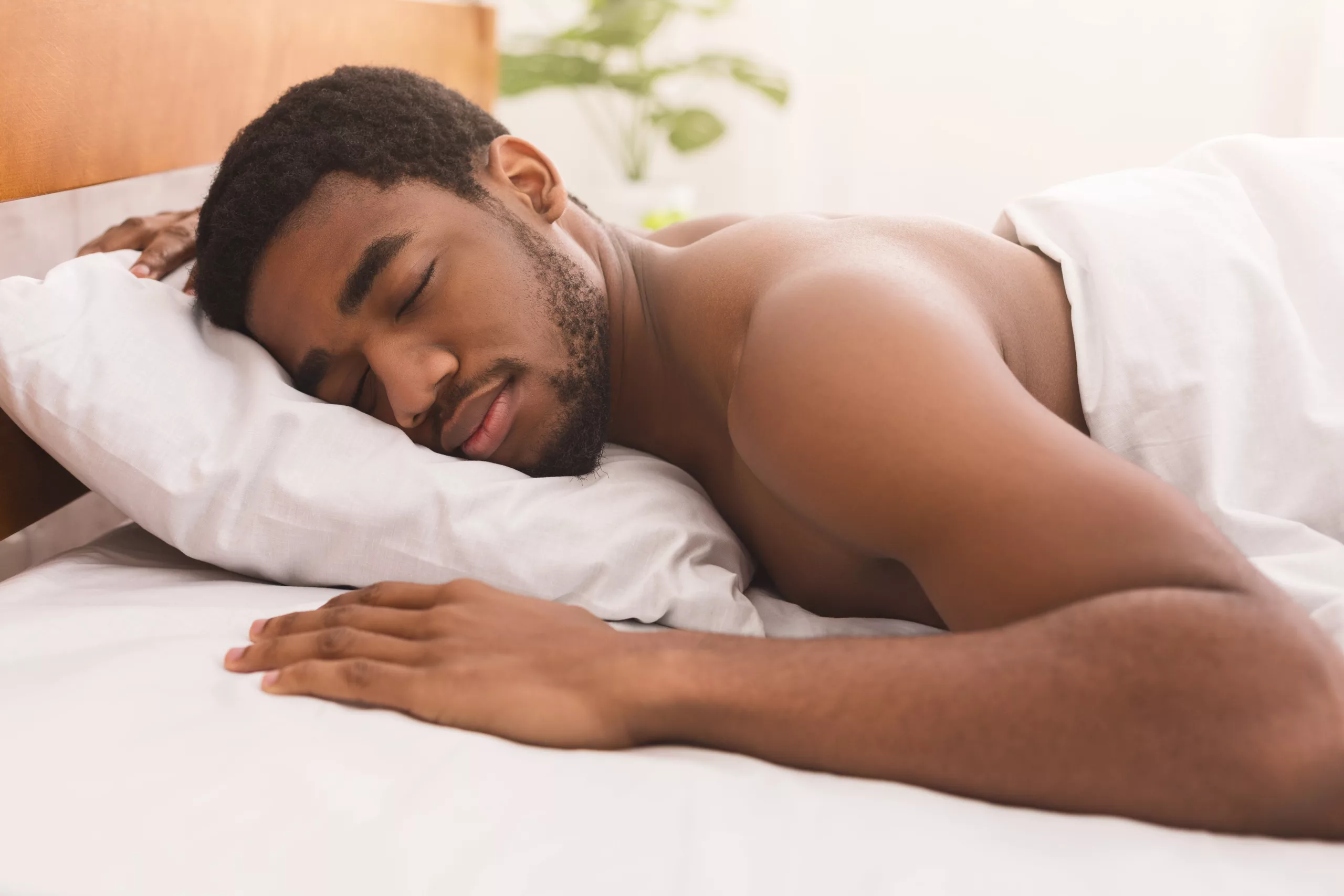 Portrait of african-american man sleeping naked on stomach in bed at home, closeup