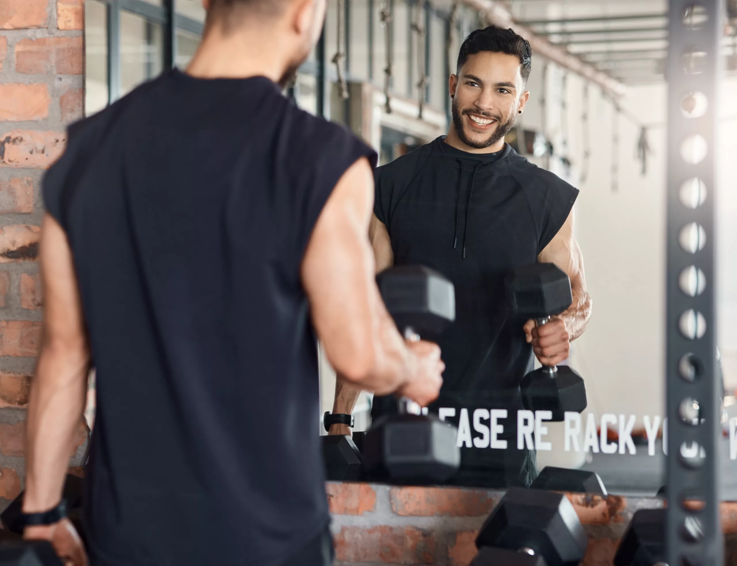 Shot of a sporty young man looking at himself in a mirror while exercising with dumbbells in a gym.