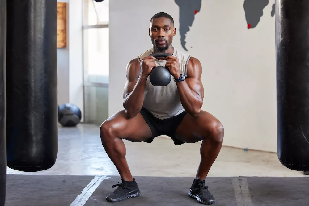 Man, kettlebell squats and exercise in gym, fitness club and sports workout. Strong athlete, bodybuilder and muscle power with weight training, lifting and energy, wellness or healthy lifestyle.